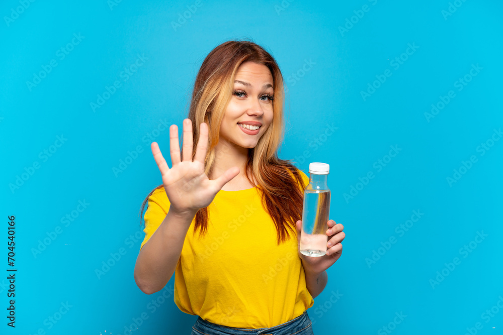 Teenager girl with a bottle of water over isolated blue background counting five with fingers