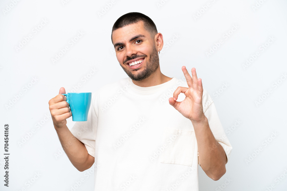Young caucasian man holding cup of coffee isolated white background showing ok sign with fingers Young caucasian man holding cup of coffee isolated white background showing ok sign with fingers