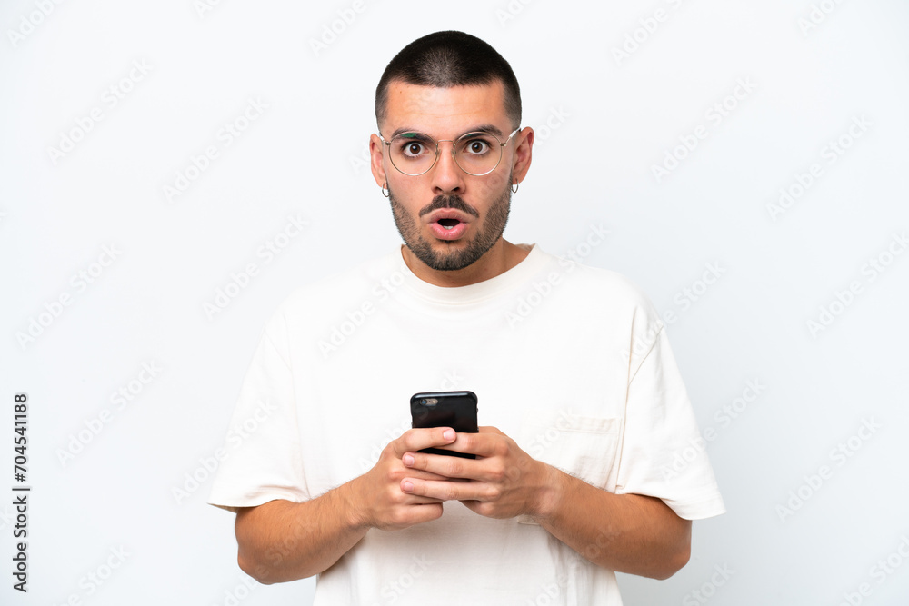 Young caucasian man isolated on white background looking at the camera while using the mobile with surprised expression Young caucasian man isolated on white background looking at the camera while using the mobile with surprised expression