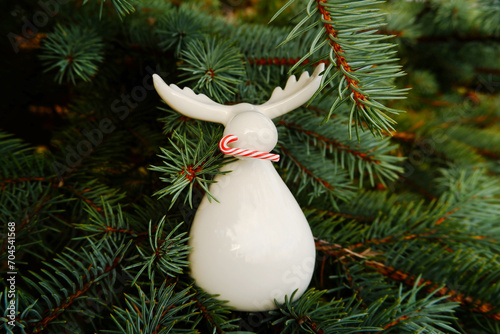 A Christmas white porcelain figurine of a moose with horns holding a red and white candy stick in its teeth among the fir branches. photo