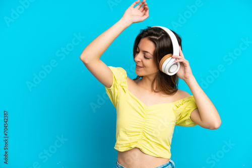 Fototapeta Naklejka Na Ścianę i Meble -  Young caucasian woman isolated on blue background listening music and dancing