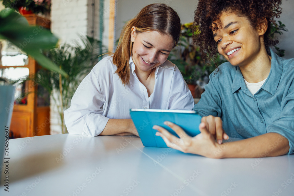 Two multiethnic female students sitting at table with tablet pc computer Two multiethnic female students sitting at table with tablet pc computer