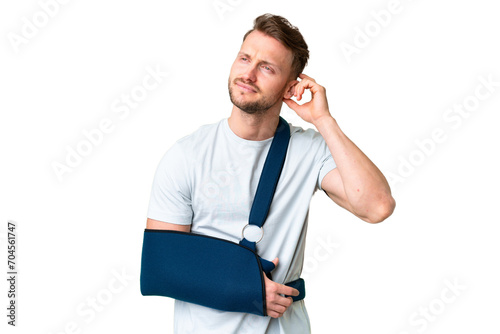 Young caucasian man with broken arm and wearing a sling over isolated chroma key background having doubts