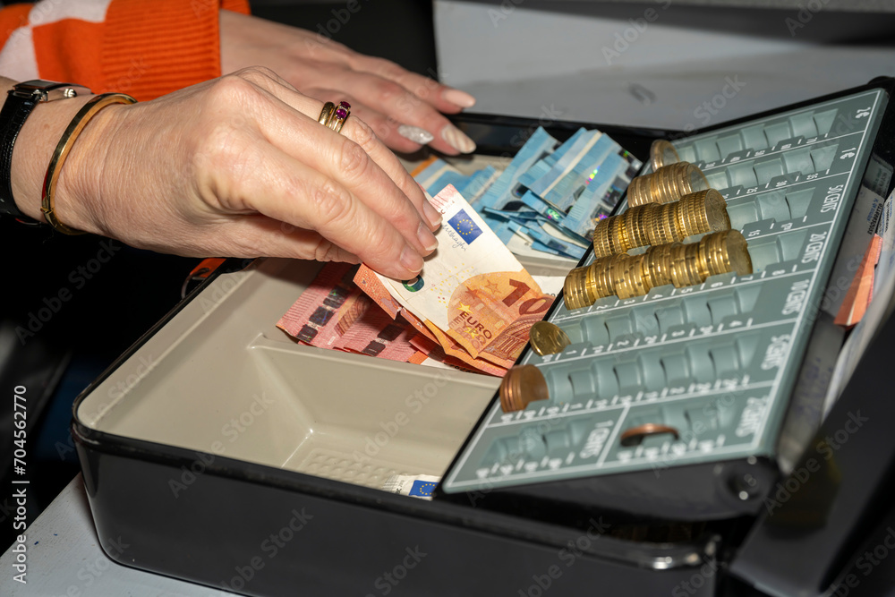 caisse enregistreuse avec des billets et des pièces en euros manipulée ...