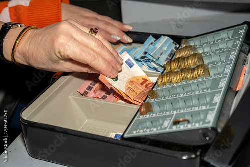 caisse enregistreuse avec des billets et des pièces en euros manipulée par une femme photo