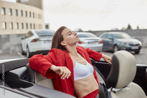 Confident relaxed young girl sitting with closed eyes on back seat in convertible