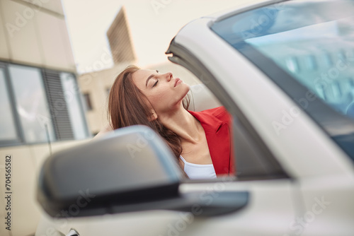Dreamy young brunette sitting with eyes closed in convertible car