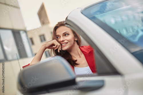 Cheerful playful young girl in red blazer enjoying summer day in convertible