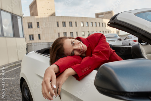Cheerful young brunette sitting in convertible with her head on hands