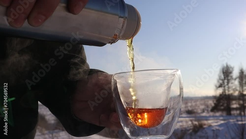 Close-up of a man pouring tea from a thermos into a mug. A sunny winter day, drinking hot tea in the cold