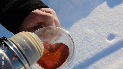 A man pours hot tea from a thermos into a clear mug. Drinking tea in winter in the cold on a sunny snowy day. There is a strong steam coming out of the mug
