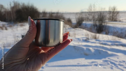 Drinking hot tea in the cold. A close-up of a mug in a woman's hand. Steam is coming from the mug, which is blown away by the winter wind.