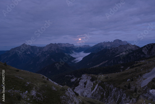Moon just before setting down shines a radiant glow on the fog in the valley. A view from the Mangart saddle towards the setting full moon. Mangart (2679 m) is a mountain in the Julian Alps.