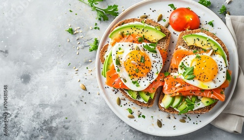 Healthy open-faced sandwiches on multigrain toast with avocado, salmon, eggs, herbs, sunflower seeds on white plate on concrete background, a plate with a sandwich and a fried egg on it with avocado. photo