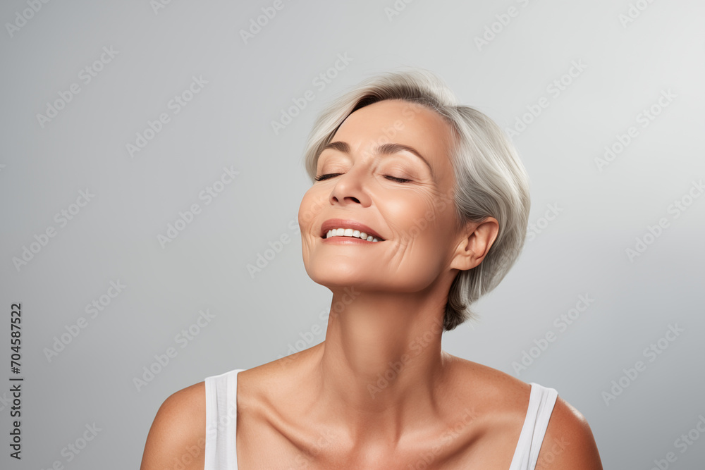 Gorgeous senior older smiling Caucasian woman with natural makeup on grey background with copy space Gorgeous senior older smiling Caucasian woman with natural makeup on grey background with copy space