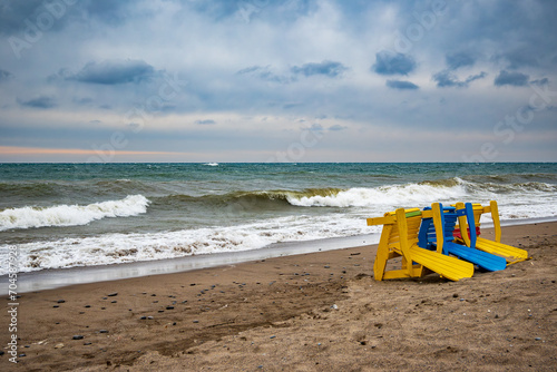 Fototapeta Naklejka Na Ścianę i Meble -  colorful beach chairs blown over by winter storm winds with dramatic breaking surf and blue clouds kew beach toronto room for text
