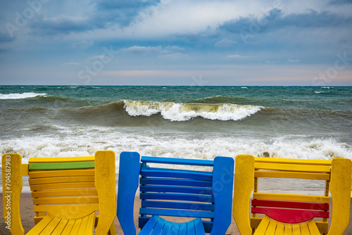 Canvas Print colorful beach chairs blown over by winter storm winds with dramatic breaking su