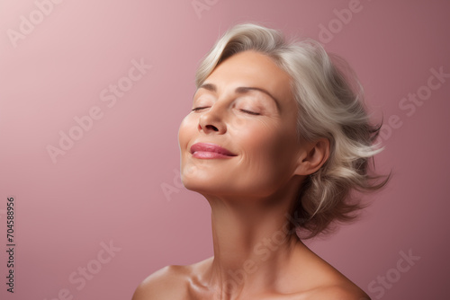 Gorgeous senior older smiling Caucasian woman with natural makeup on pink background with copy space