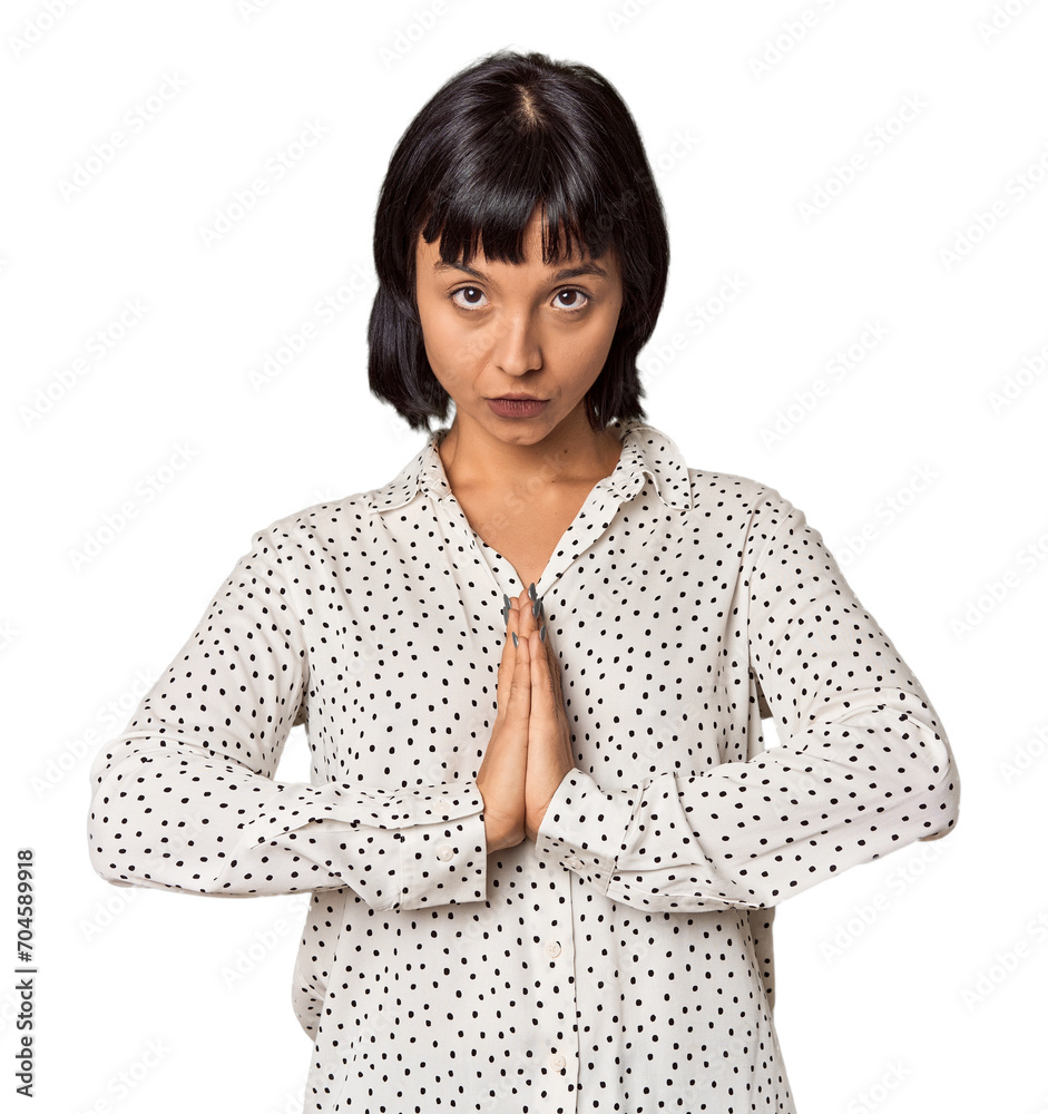 Young Hispanic woman with short black hair in studio praying, showing devotion, religious person looking for divine inspiration.