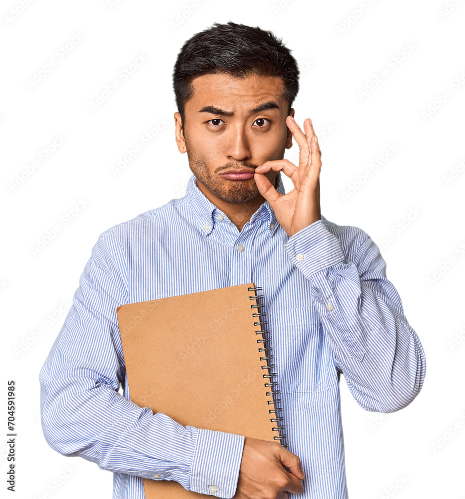 Chinese student with a notebook in studio with fingers on lips keeping a secret. Chinese student with a notebook in studio with fingers on lips keeping a secret.