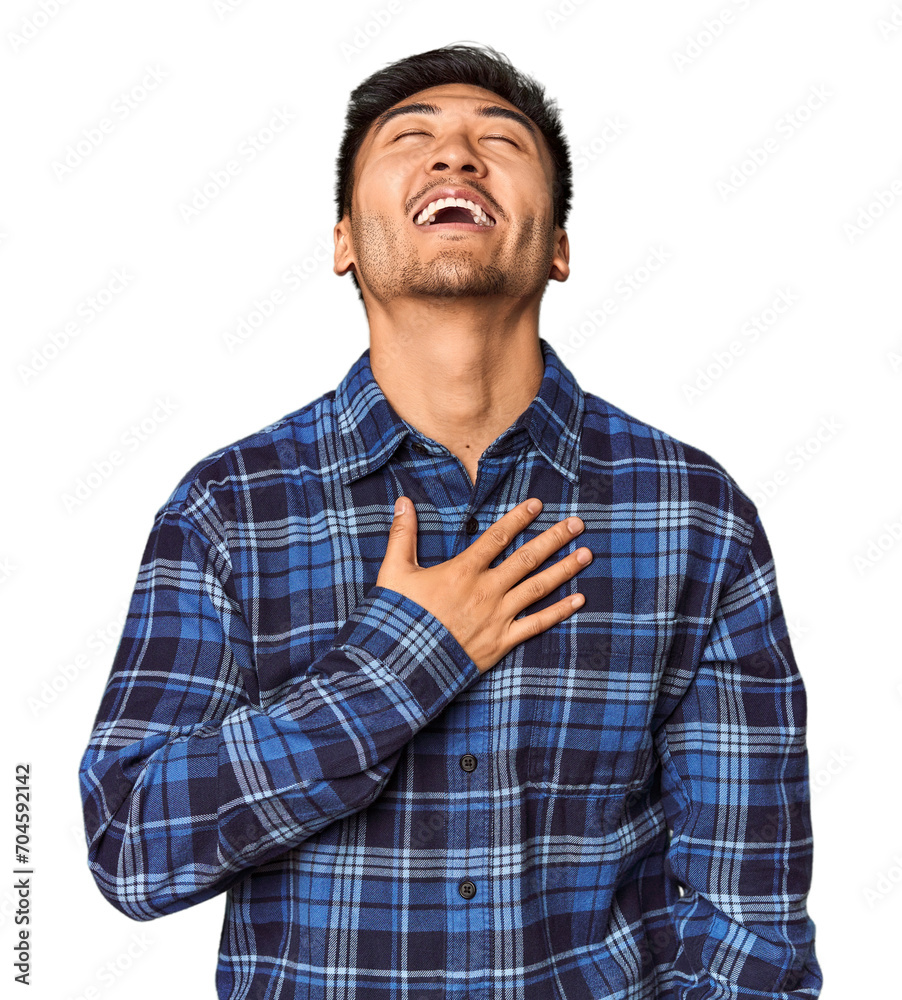 Young Chinese man in studio background laughs out loudly keeping hand on chest. Young Chinese man in studio background laughs out loudly keeping hand on chest.