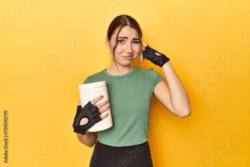 Fit woman holding a protein shake showing a disappointment gesture with forefinger.