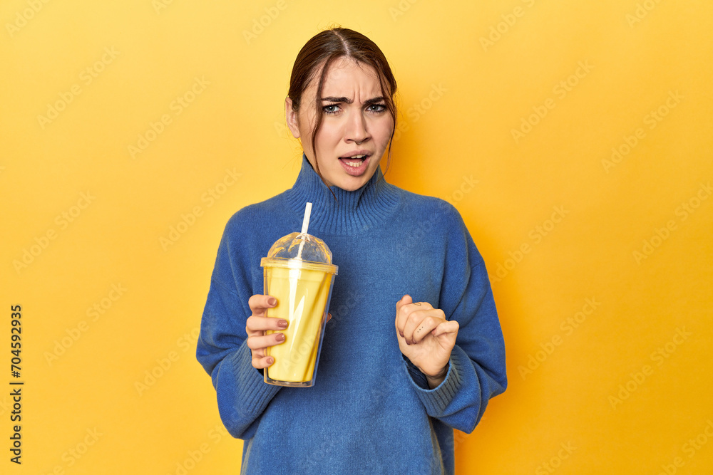 Young caucasian woman enjoying a creamy vanilla shake screaming very angry and aggressive. Young caucasian woman enjoying a creamy vanilla shake screaming very angry and aggressive.