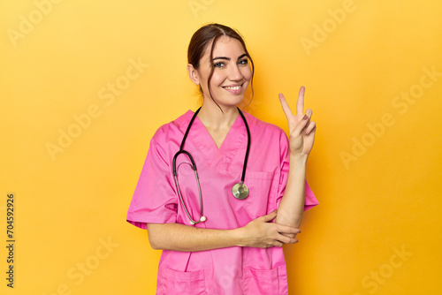 Nursing assistant in yellow background showing number two with fingers.