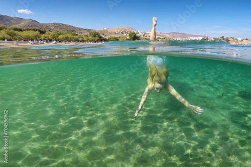 Young woman swims at the bottom of the beach Livadakia on half underwater view in Serifos, Greece