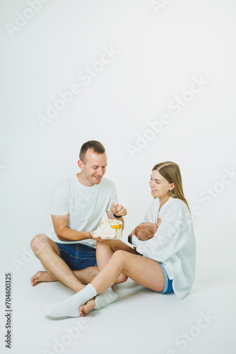 Young happy parents with a baby in their arms and a cake celebrate the first month of the baby's life. Mom and dad with a newborn baby on a white background