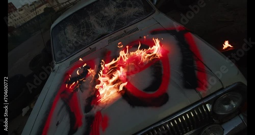 Fire dangerous burning on the destroyed with cruel old car's bonnet, painted bright red signature riot. A broken car at dawn time and flame reminding about violent street protests actions photo