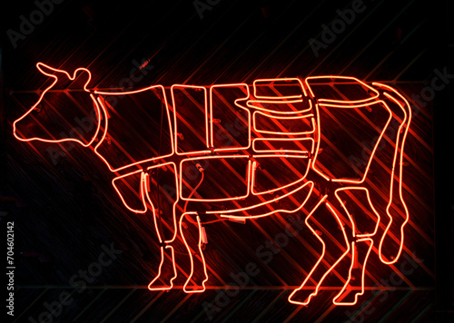 Neon sign of a cow and cutting beef into meat parts. photo