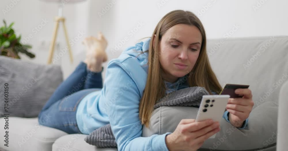 Woman relaxes on couch holding a smartphone and credit card, doing e-commerce Woman relaxes on couch holding a smartphone and credit card, doing e-commerce