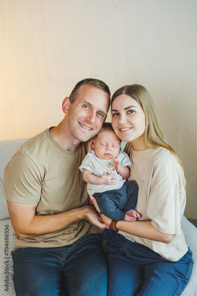 Young happy parents with a newborn baby in their arms at home on the couch. Mom and dad with a newborn baby on a white background Young happy parents with a newborn baby in their arms at home on the couch. Mom and dad with a newborn baby on a white background