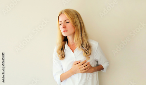 Young woman grabbing put hands on her chest suffering from heart pain, feeling bad with acute pain in office photo