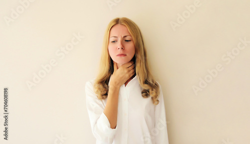 Sick exhausted young woman touches her neck with hand while suffering from acute sore in throat flu, she feels bad photo