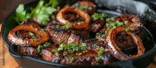 Filipino dry aged angus bistek tagalog steak with onion rings in soy sauce, served in a cast-iron casserole. photo
