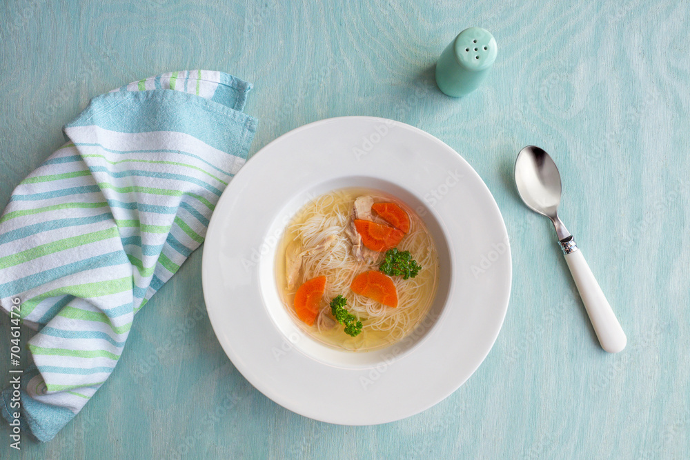 Clear chicken broth with pieces of meat, carrot, parsley and noodles. Top view. StockFoto