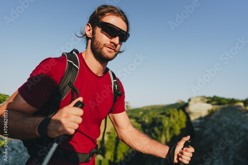 Young man hiker travels through the mountains with trekking poles for nordic walking