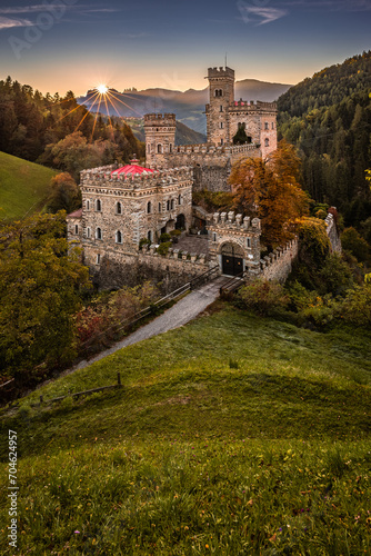 Latzfons, Italy - Beautiful autumn scenery at Gernstein Castle (Castello di Gernstein, Schloss Gernstein) at sunrise in South Tyrol with blue sky and golden foliage and flowers at foreground