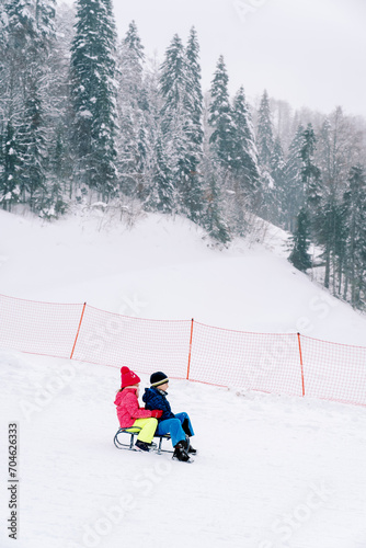 Little boy and girl are sledding down the slope of a snowy mountain