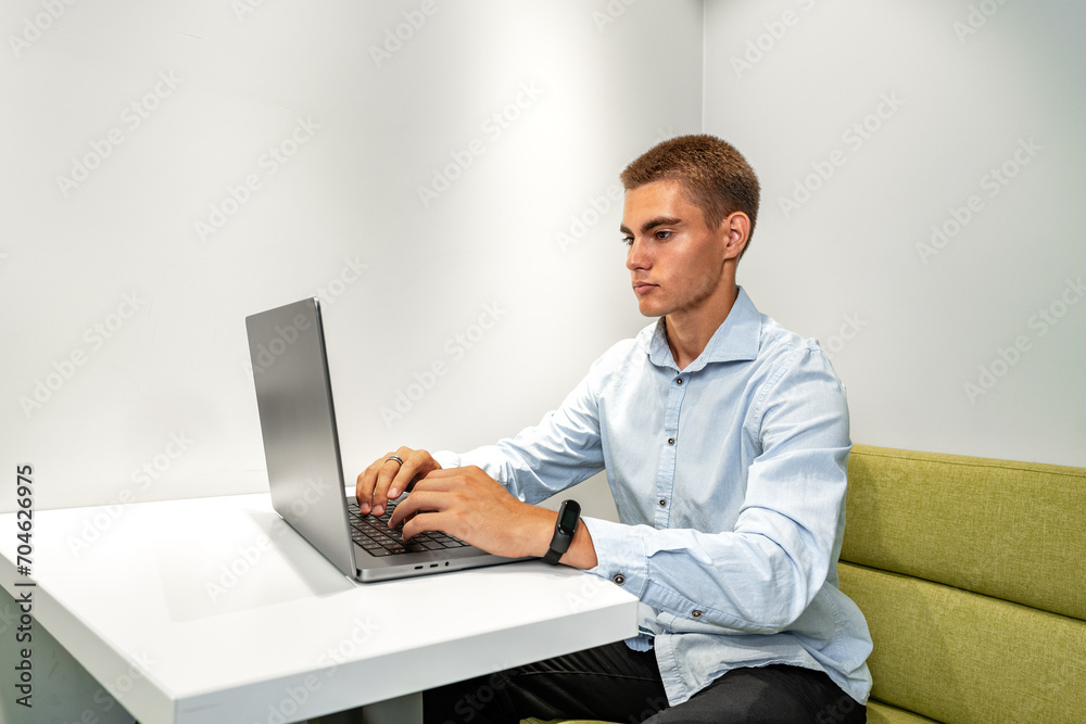 Handsome young businessman sitting in office lobby with a laptop Handsome young businessman sitting in office lobby with a laptop