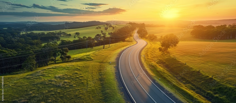 Fototapeta premium Sunset view of Australian countryside road passing agricultural land captured from above.