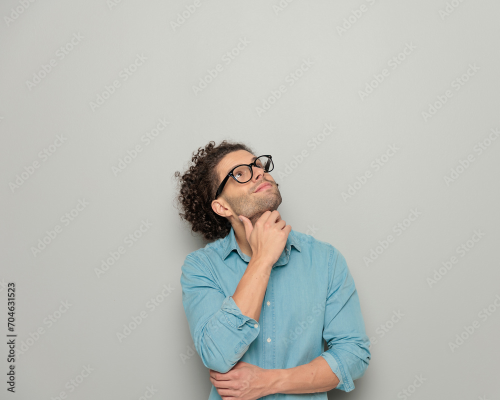 cute young man with glasses touching chin, looking up and dreaming cute young man with glasses touching chin, looking up and dreaming