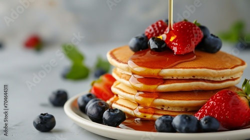 Pancakes with fresh strawberries, blueberry and maple syrup for a breakfast, honey pouring on delicious homemade pancakes with copy space.
