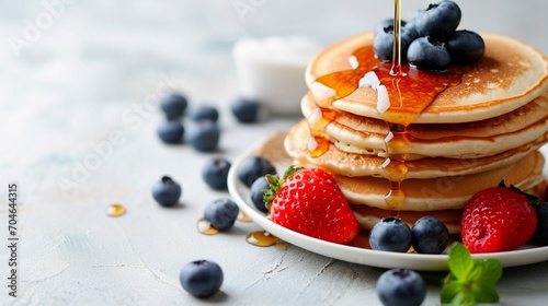 Pancakes with fresh strawberries, blueberry and maple syrup for a breakfast, honey pouring on delicious homemade pancakes with copy space. photo