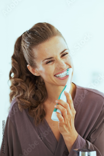 woman brushing teeth with electric toothbrush in bathroom