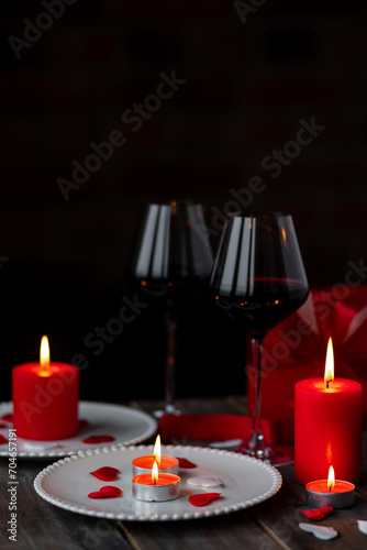 Saint Valentine's Day celebration. Red burning candles, hearts, gift box, postcard on dark wooden background. Happy holiday . Table decor for festive dinner, romantic atmosphere. Copy space for text