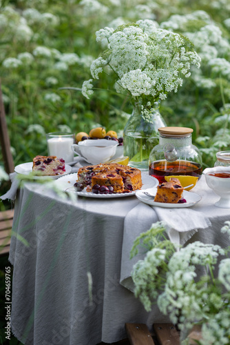 Fototapeta Naklejka Na Ścianę i Meble -  Tea time with sweet homemade cherry cake and herbal beverage in summer garden outdoors. Table covered with linen tablecloth, white porcelain cups. English style