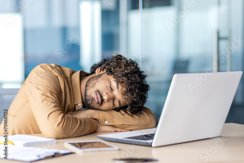Businessman sleeping at workplace, young overtired and overworked man lying on desk inside office with laptop, long work until late, deadline in evening. photo